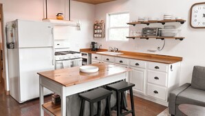 A modern kitchen with white cabinetry, a wooden countertop, and a built-in stove. There are two black stools and a small table. - Tranquility Heights: Deck, 3.5 acres, Darts, Movie Room, Desk w/Printer (Ozark)