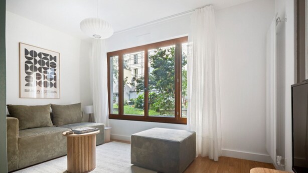 Un salon moderne comprenant un canapé, un pouf, une table basse et une grande fenêtre avec des rideaux.
