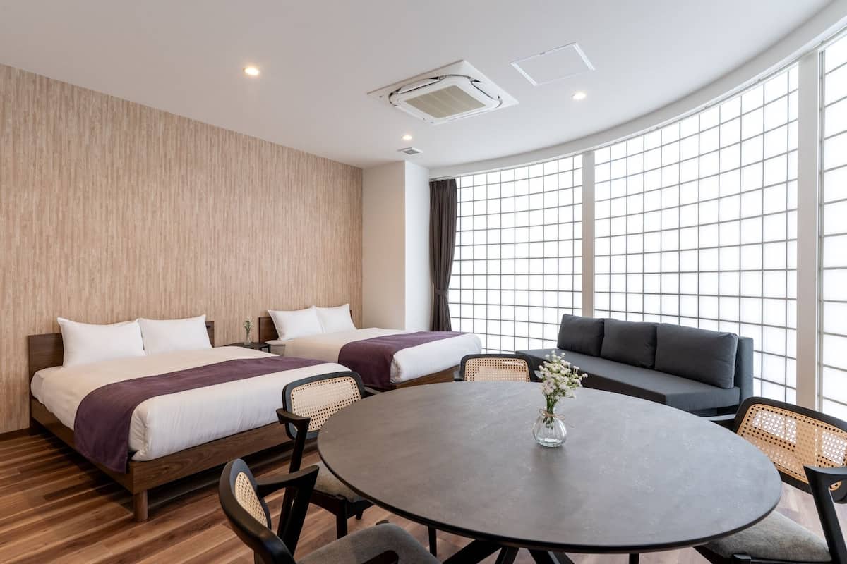 Quarto de hotel com duas camas, uma mesa redonda e um sofá.