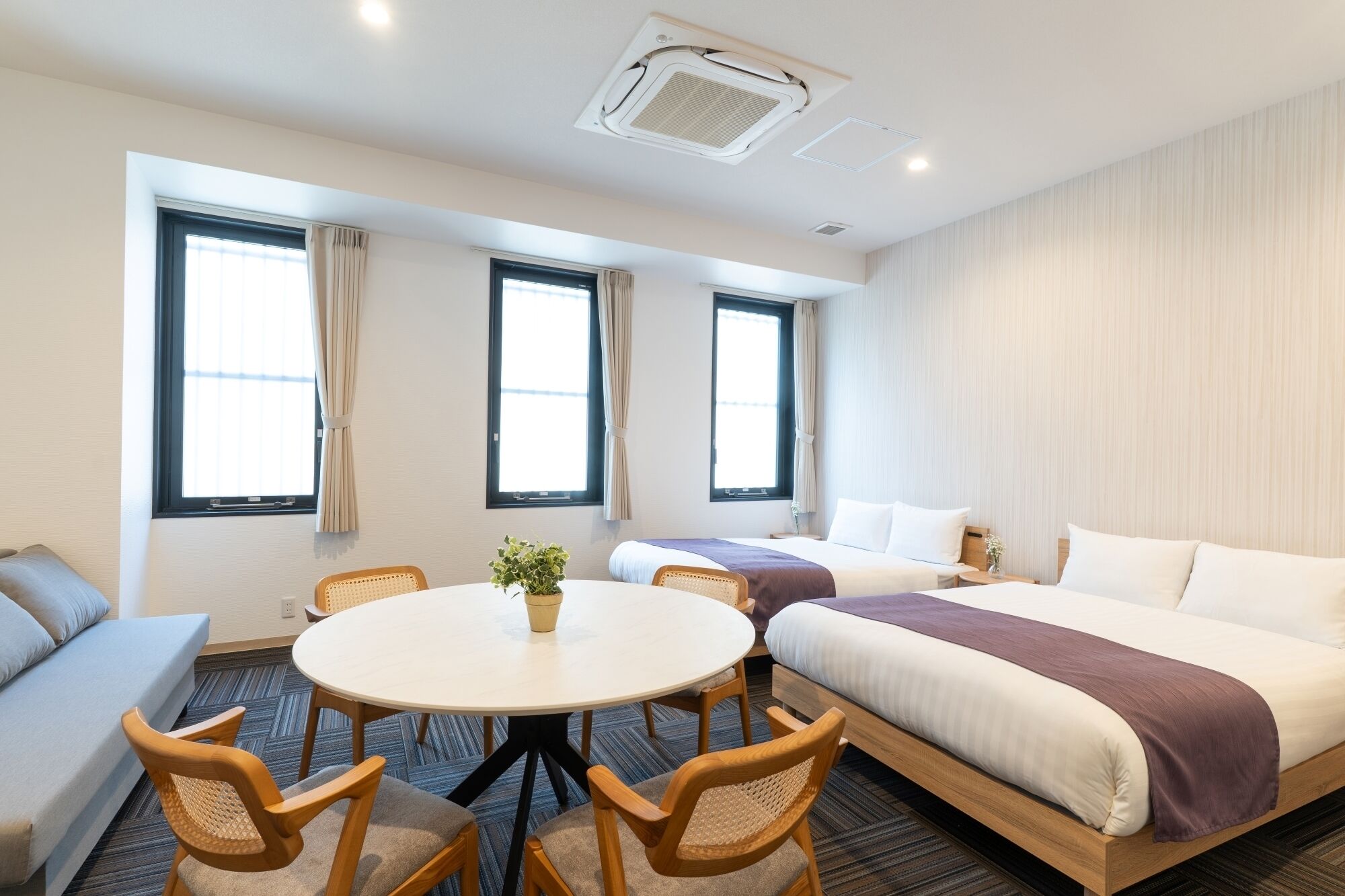 Ein Hotelzimmer mit einem runden Tisch, vier Stühlen, zwei Betten und großen Fenstern.