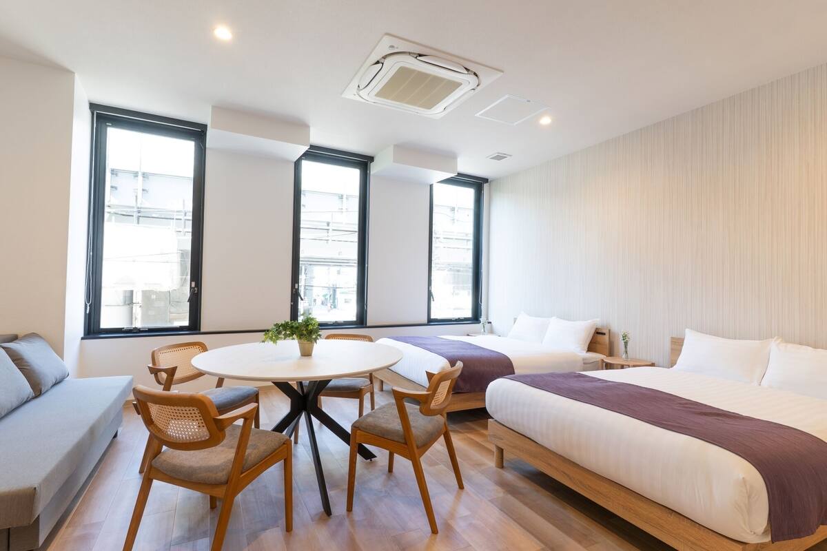 Quarto de hotel moderno com uma cama grande, uma cama menor, uma mesa de jantar redonda com cadeiras e um vaso com planta.