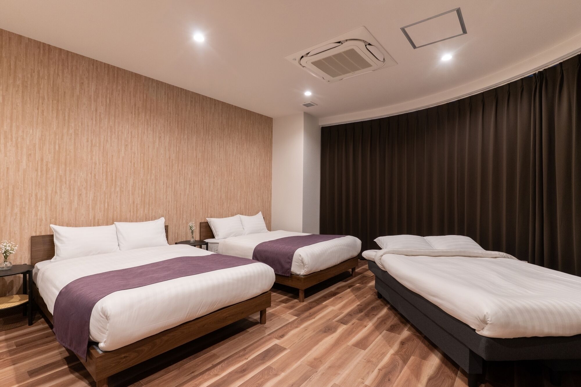 Quarto de hotel com duas camas, soalho de madeira, cortina escura e ventilação no teto.