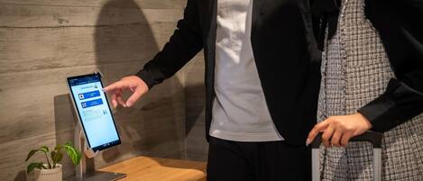 A person interacting with a digital kiosk in a modern setting with a wooden bench and a potted plant.
