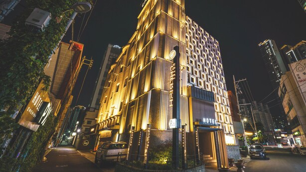 Un hotel de diverses plantes amb un disseny modern, amb cartelleria il·luminada i un logotip destacat a la part superior.
