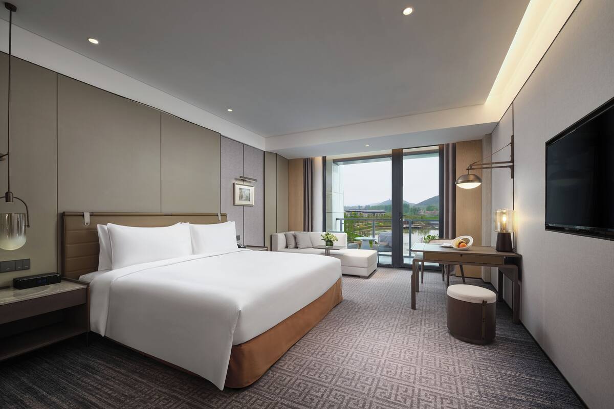 Habitación de hotel moderna con una cama grande, un escritorio con silla, televisión y balcón con vistas al exterior.