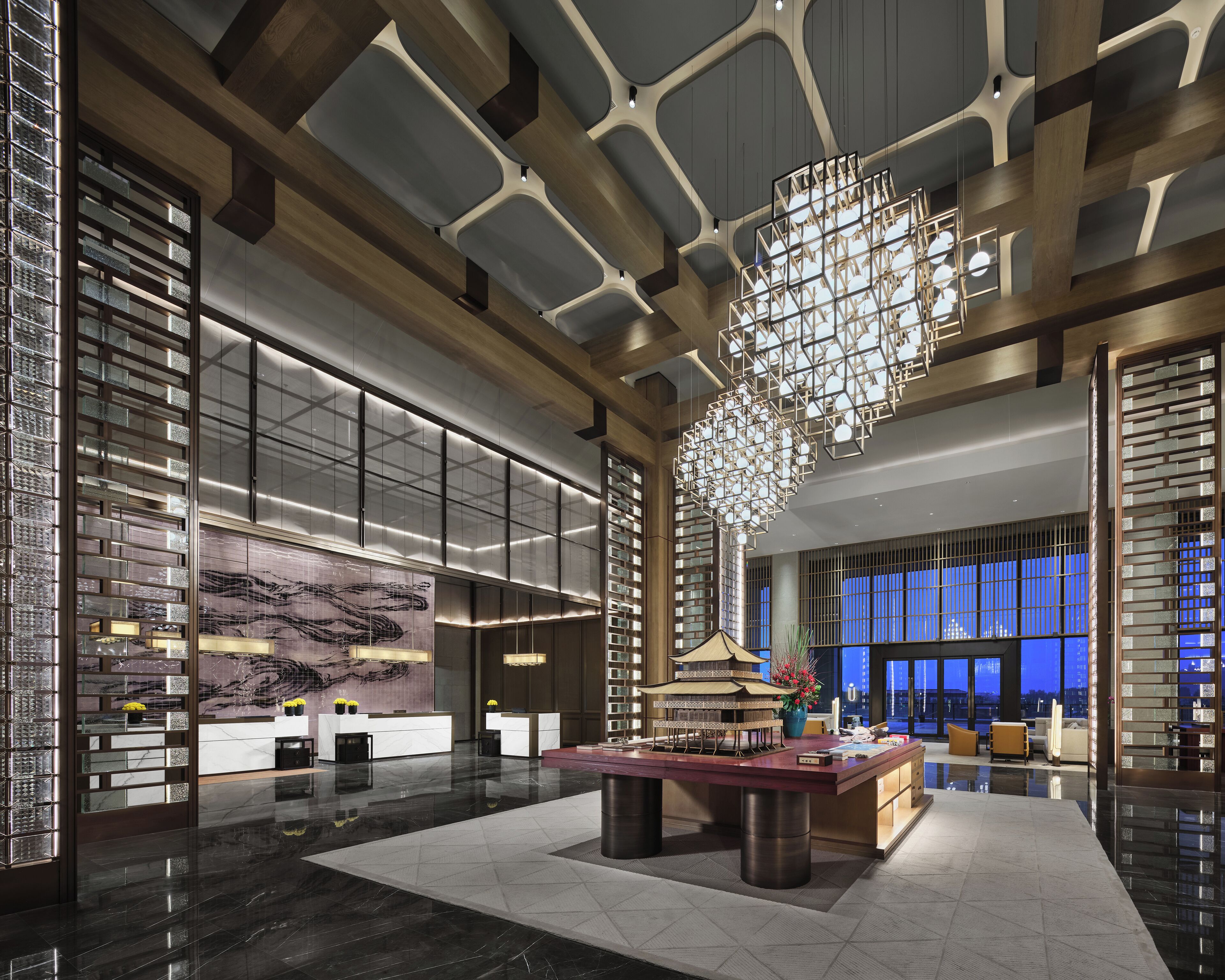 A spacious lobby with a central reception desk, modern chandeliers, and large windows offering views of the cityscape.