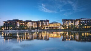 A hotel with multiple buildings, a reflective water body in front, and a clear sky. - Primus Hotel Xuzhou Dalong Lake (Xuzhou)