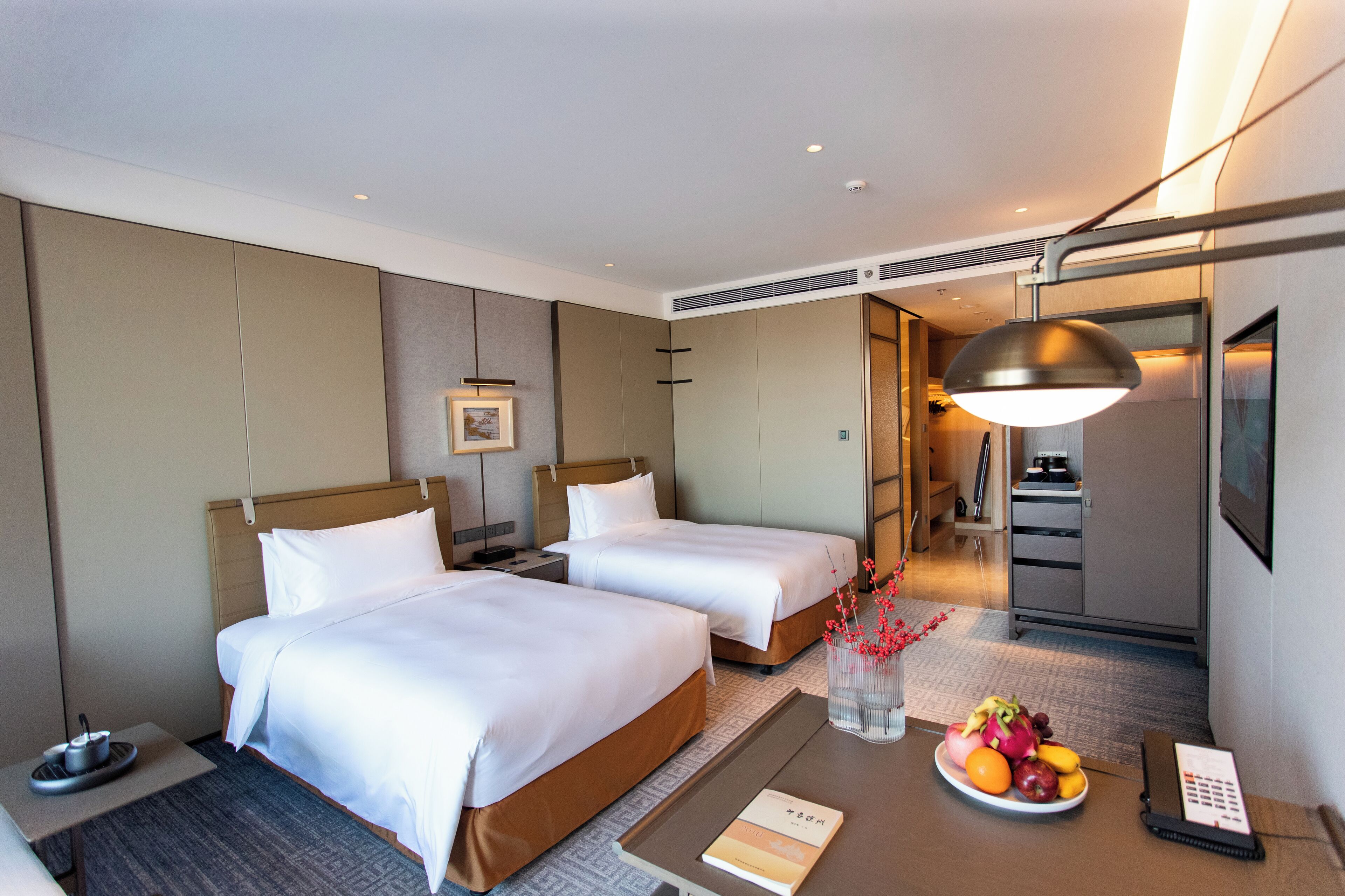 Habitación de hotel con dos camas, un escritorio con frutero, una lámpara y un teléfono.