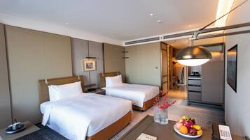 Habitación de hotel con dos camas, un escritorio con frutero, una lámpara y un teléfono.