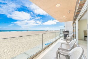 Ein Balkon mit Blick auf einen Strand, einem Grill und einer Sitzgelegenheit.
