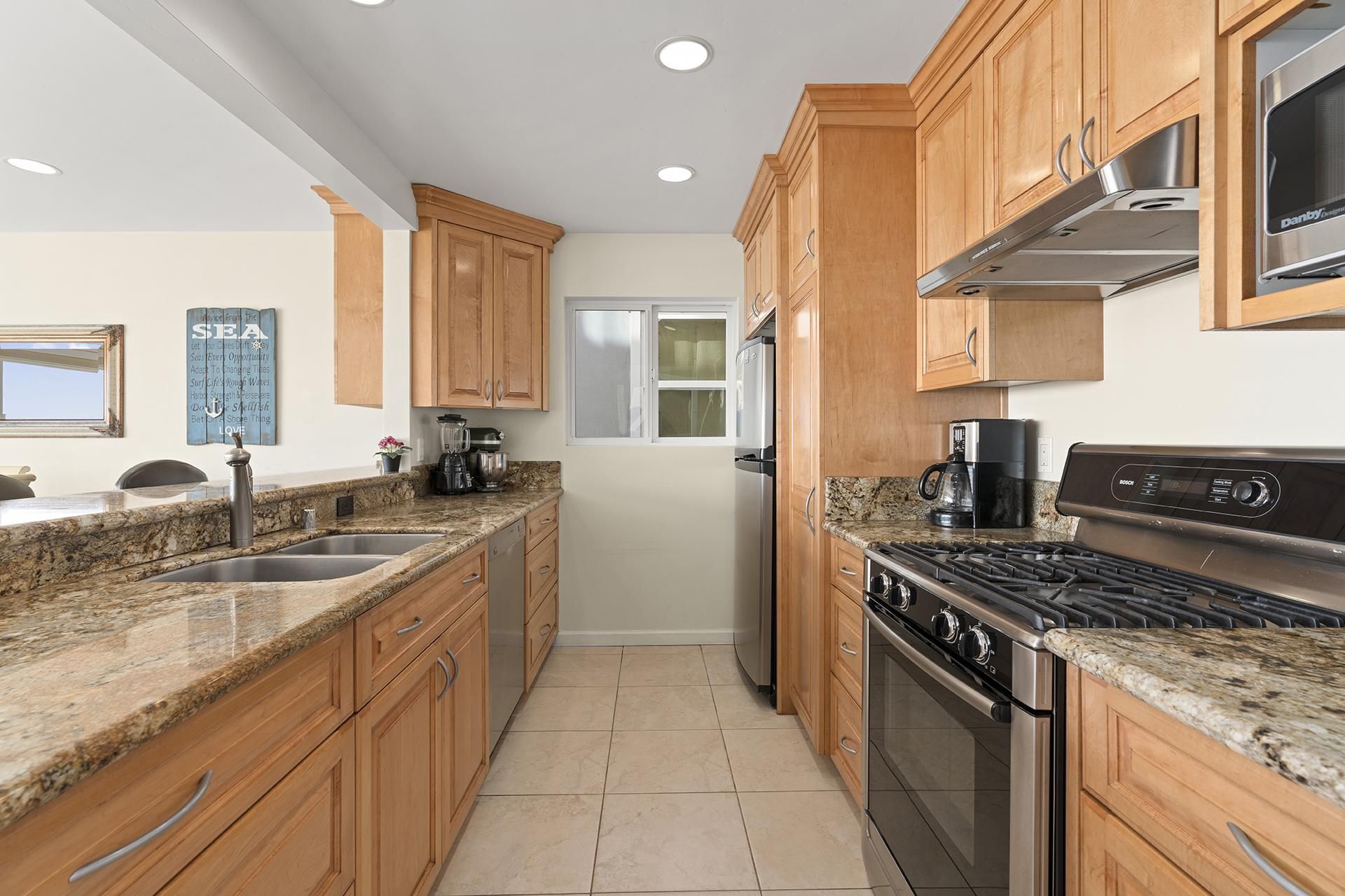 A modern kitchen with wooden cabinets, granite countertops, stainless steel appliances, and a window providing natural light.