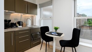 A modern kitchen with stainless steel appliances, a dining area with two black chairs, and a window with a view of the city. - GuestReady - Cosy studio in central Greenwich (London)
