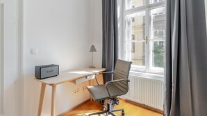 Una habitación con escritorio, silla, lámpara y ventana con cortinas.