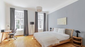 Un dormitorio moderno con una cama de madera, un escritorio con una silla, una lámpara de pie y vistas al exterior a través de amplias ventanas.