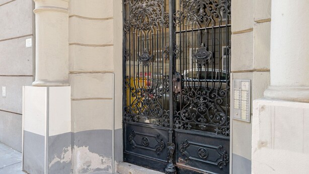 A wrought iron gate with intricate designs, a column, and a utility box on the wall. - Blueground | Landstraße, view, nr Belvedere (Vienna)