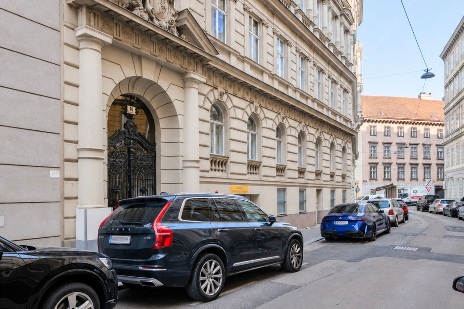 Une rue bordée de voitures garées et un bâtiment à l’architecture classique.