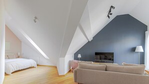 A modern loft bedroom with a sloped ceiling, a large bed, a sofa, and a TV. - Blueground | Landstraße, view, nr Belvedere (Vienna)