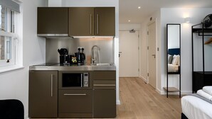 Una cocina compacta con horno integrado, microondas y fregadero, una cafetera pequeña y una ventana con cortinas.