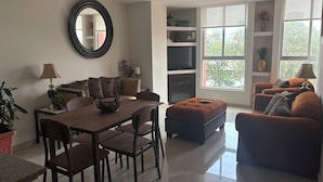 A modern living room with a dining area, a fireplace, and large windows offering a view of the outdoors. - Cozy apartment close to everything CDMX! (Ciudad de México)
