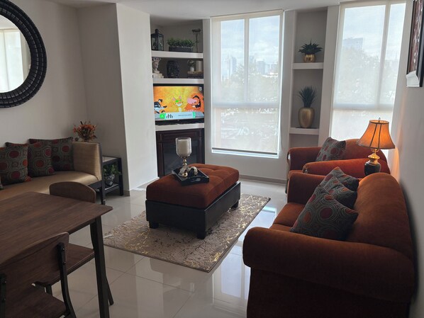 Ein modernes Wohnzimmer mit einer Couch, einem Hocker, einem Couchtisch und einem Fernseher auf einem Schrank.