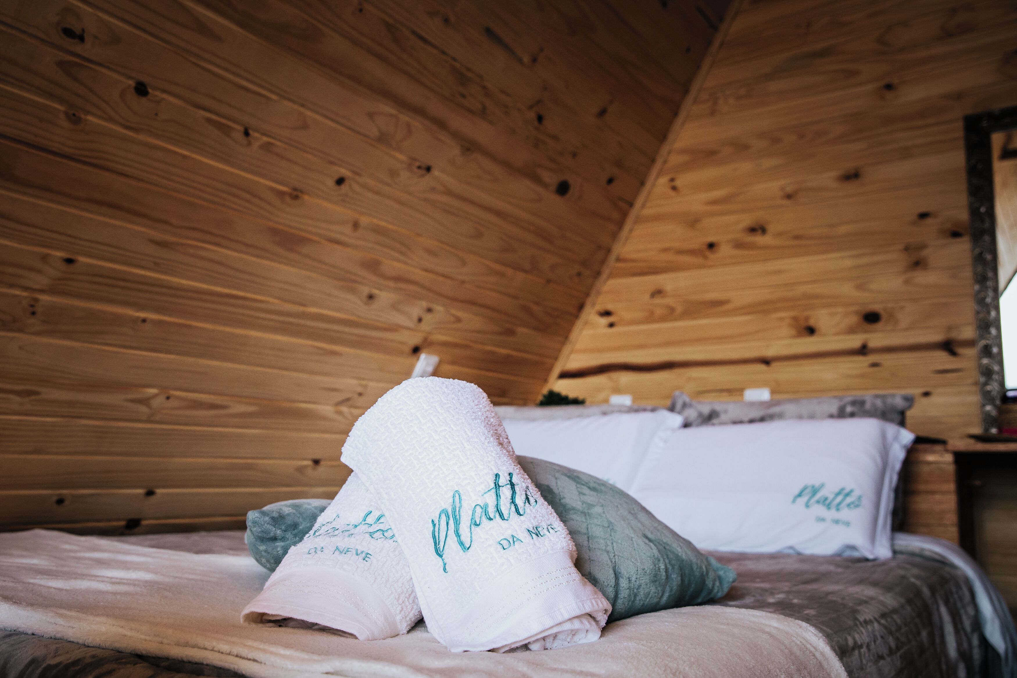A wooden cabin interior with a bed, pillows, and towels.