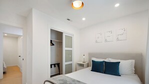A modern bedroom with a large bed, a walk-in closet, and a bedside table with a lamp.