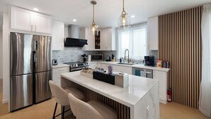 A modern kitchen with a stainless steel refrigerator, a central island with bar stools, a microwave, a stove, and a sink.