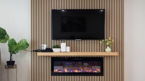 A modern living room with a flat-screen TV mounted above a fireplace, flanked by wooden paneling.