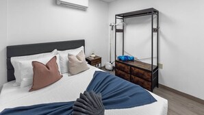 Una habitación de hotel con una cama, un tocador de madera, un espejo y un equipo de aire acondicionado.