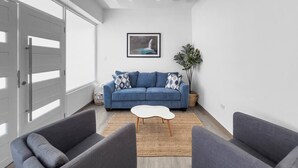 Una sala de estar moderna con un sofá azul, dos sillones, una mesa de centro blanca y un gran ventanal con vistas a una cascada.