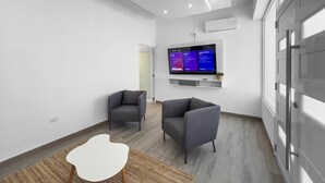 Una sala de estar moderna con dos sillones grises, una mesa de centro blanca y un televisor de pantalla plana montado en la pared.