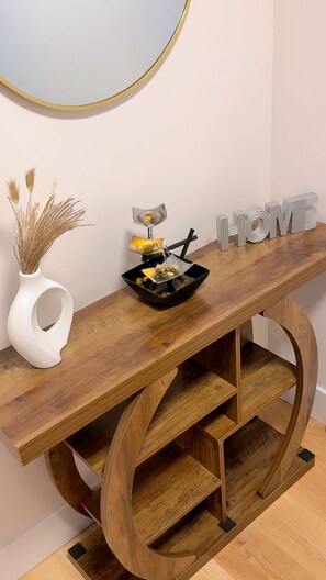 Una consola de madera con un cuenco de objetos decorativos y un florero con plantas secas.