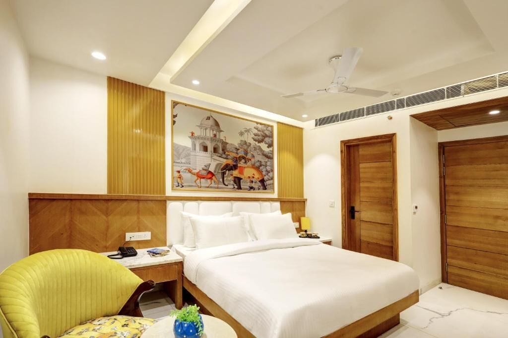 A hotel room with a bed, a desk, a chair, a painting on the wall, and wooden doors.