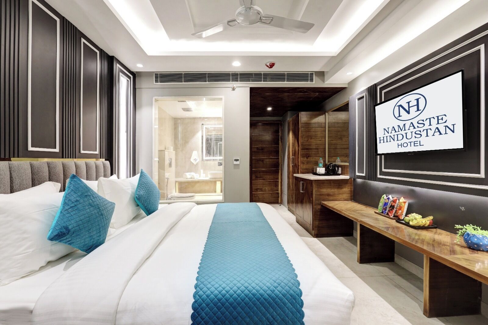Una habitación de hotel moderna con una cama grande, una mesita de noche con aperitivos, un espejo y un letrero con el nombre del hotel.