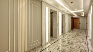 Een hotelgang met marmeren vloeren, witte paneelbekleding en inbouwverlichting.