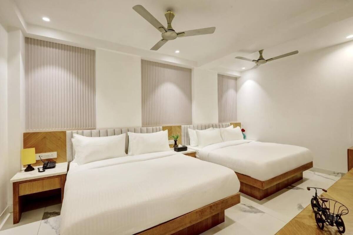 Quarto de hotel com duas camas, cabeceira de madeira, mesas de cabeceira com abajures e ventiladores de teto.