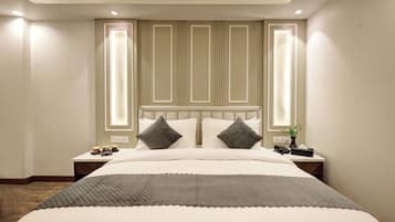 A modern hotel room with a large bed, two bedside tables, and a nightstand with a lamp.