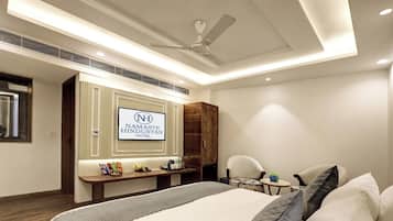 Una habitación de hotel con una cama, un escritorio, una silla, un ventilador de techo y un cartel del Hotel Namaste Hindustan.
