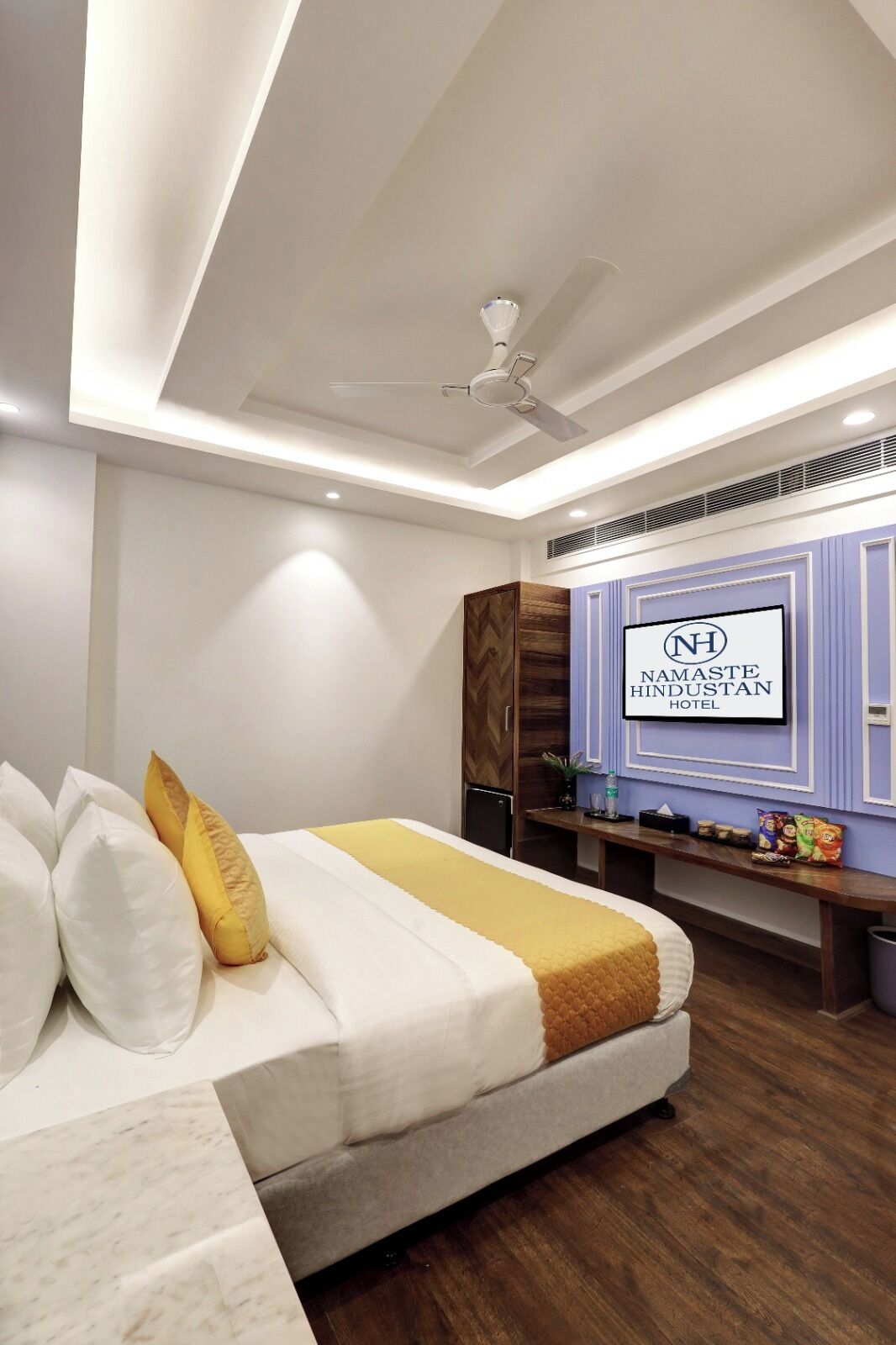 A hotel room with a bed, a ceiling fan, a TV mounted on the wall, and a wooden cabinet.
