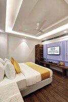 Una camera d'albergo con un letto, una ventola a soffitto, una TV fissata al muro e un mobiletto in legno.