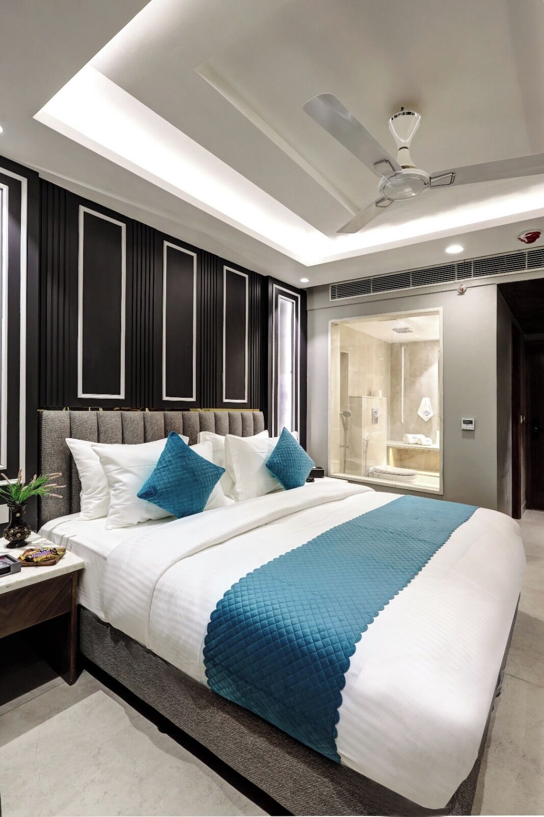 Ein modernes Hotelzimmer mit einem großen Bett, einem Deckenventilator und einer bodengleichen Dusche.