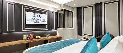 A hotel room with a bed, a bedside table with snacks, a TV mounted on the wall, and a ceiling fan.