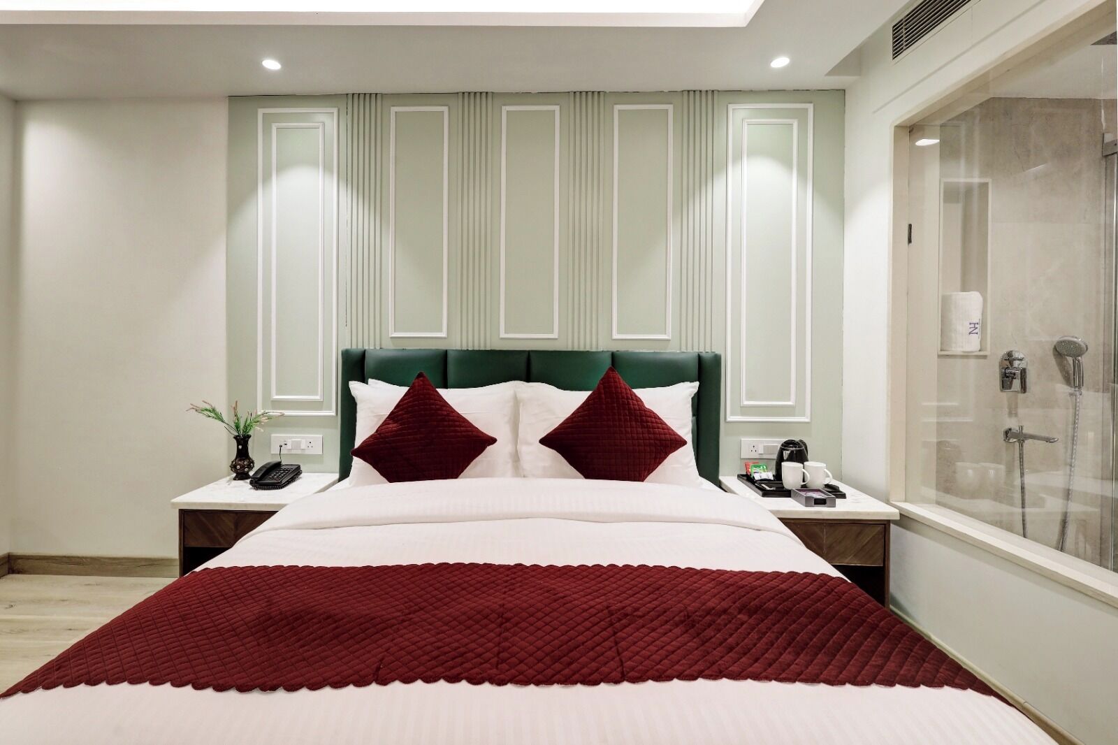 A hotel room with a large bed, a nightstand with a phone and a plant, a shower area, and a green headboard.