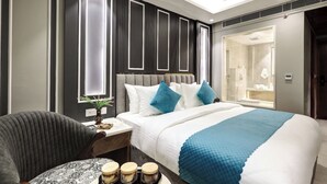 Een moderne hotelkamer met een groot bed, een nachtkastje met een vaas en kaarsen, een stoel en uitzicht op de badkamer.
