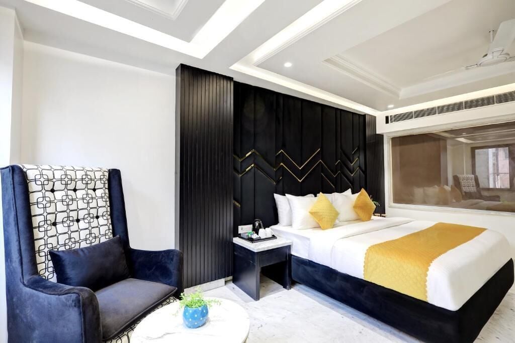 A modern hotel room with a large bed, a dark accent wall, a seating area with a chair, and a small side table.