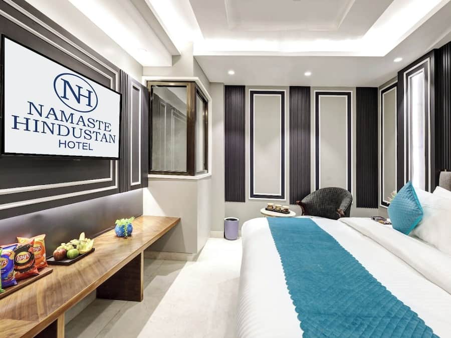 Une chambre d’hôtel équipée d’un lit, d’un bureau avec des collations, d’une chaise et d’un téléviseur affichant le nom de l’hôtel.