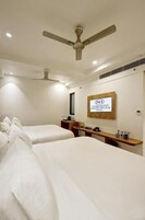 A hotel room with two beds, a ceiling fan, a wall-mounted TV, and a sign for the Namaste Hindustan Hotel.