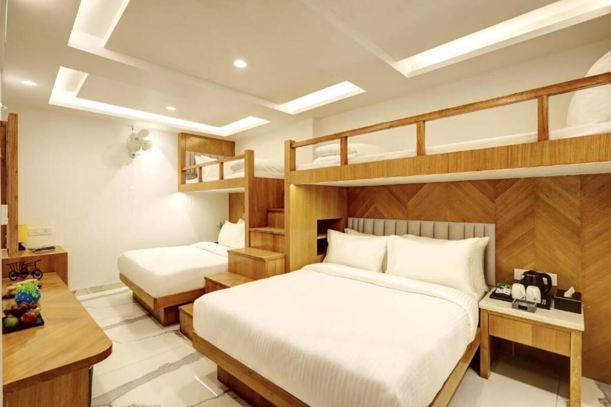 Quarto de hotel moderno com uma cama grande, uma cama menor, uma mesa de trabalho com cadeira e um espelho.