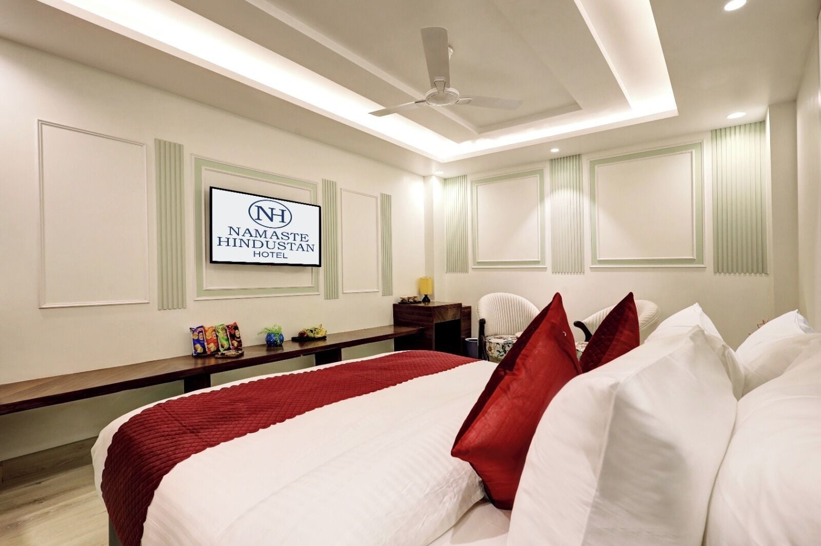 Una habitación de hotel con una cama grande, un escritorio y un televisor que muestra el nombre del hotel.