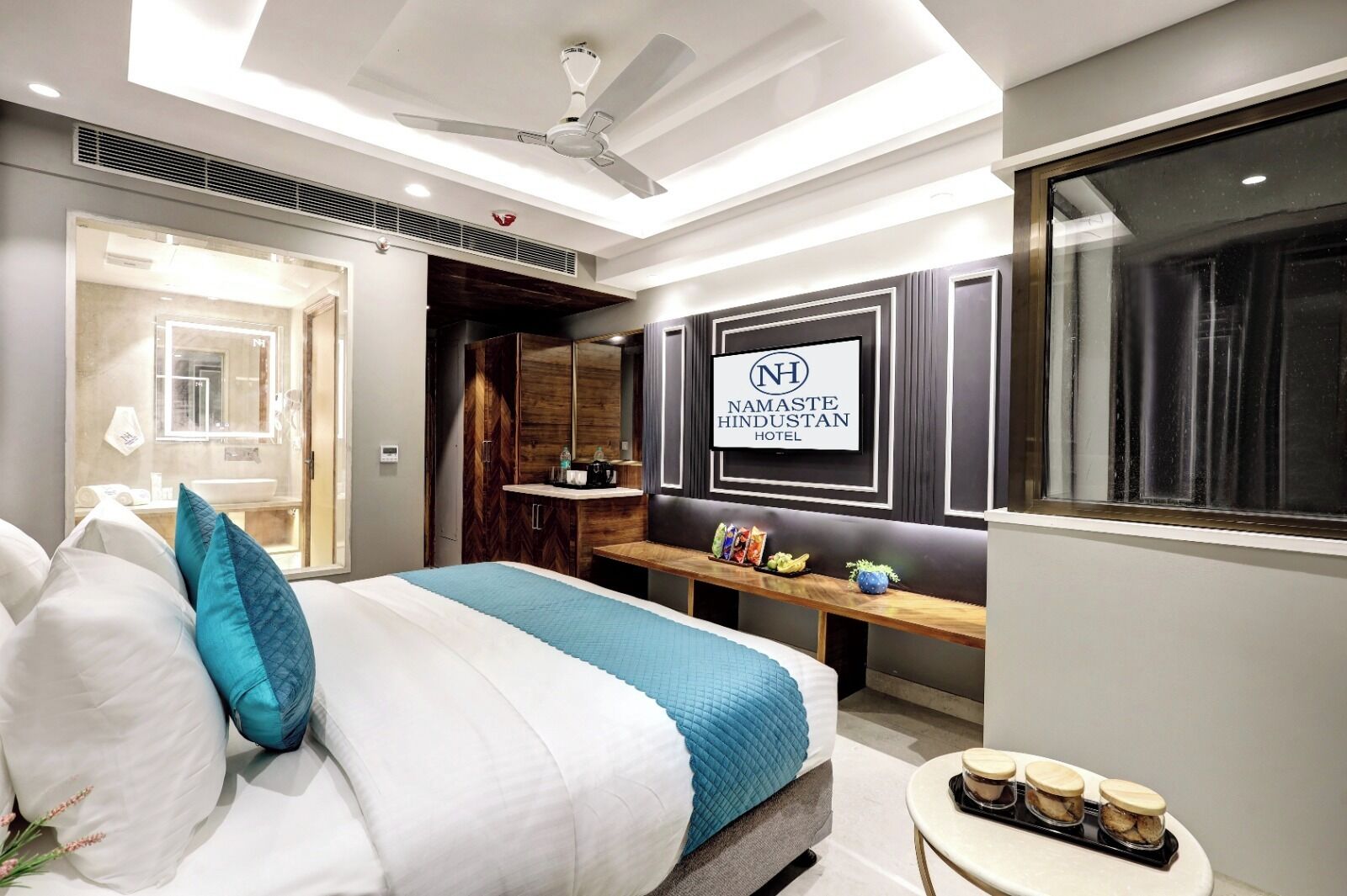 A modern hotel room with a bed, a vanity, a bench with snacks, and a ceiling fan.
